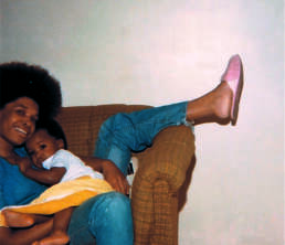 Black woman with afro laying in a chair holding her infant son